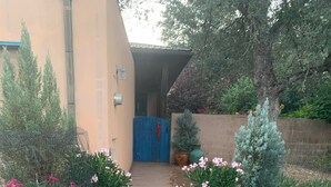 A gravel pathway leading to a building entrance with a blue door. There are potted plants with pink flowers on either side of the path. - Heidi's Artistic Abode, peaceful relaxation! (Three Rivers)