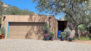 A single-story building with a garage door, surrounded by gravel and potted plants. - Heidi's Artistic Abode, peaceful relaxation! (Three Rivers)