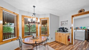 Une cuisine avec des meubles de rangement en bois, une table à manger avec des chaises, un lustre et un coin café.