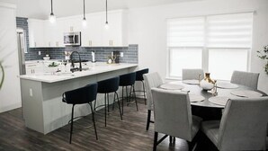 A modern kitchen with a central island, bar stools, and a dining table with chairs. - Family Getaway ~Renovated 3BR Home+ Private Pool Close to Airport, DT, & F1 (Austin)