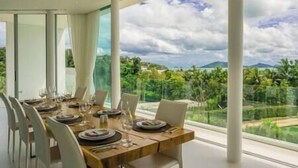 A dining area with a table set for four, large windows offering a view of a lush landscape.