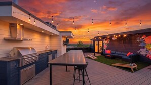 A modern outdoor kitchen with a grill, bar stools, and a dining table. - Rooftop w/ Skyline Views & Outdoor Kitchen-15 Min to Broadway-Family Friendly (Nashville)