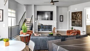 A modern living room with a sofa, coffee table, and TV. There's a staircase with a railing and a ceiling fan. - Rooftop w/ Skyline Views & Outdoor Kitchen-15 Min to Broadway-Family Friendly (Nashville)