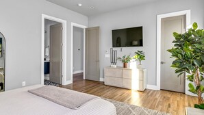 A modern bedroom with a large bed, a dresser, a TV, and a plant. - Rooftop w/ Skyline Views & Outdoor Kitchen-15 Min to Broadway-Family Friendly (Nashville)