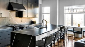 A modern kitchen with dark cabinetry, a central island with bar stools, and a large window providing natural light. - Rooftop w/ Skyline Views & Outdoor Kitchen-15 Min to Broadway-Family Friendly (Nashville)