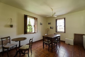 A dining area with a round table and four chairs, two windows with curtains, a ceiling fan, and a radiator. - Quinta do Pomarinho - Quarto Twin Eras - by Rowdhouses 432668 (Arouca)