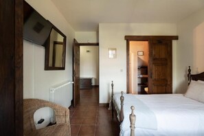 A bedroom with a wooden bed, a wicker chair, a radiator, and a wooden door leading to a staircase. - Quinta do Pomarinho - Quarto Twin Eras - by Rowdhouses 432668 (Arouca)