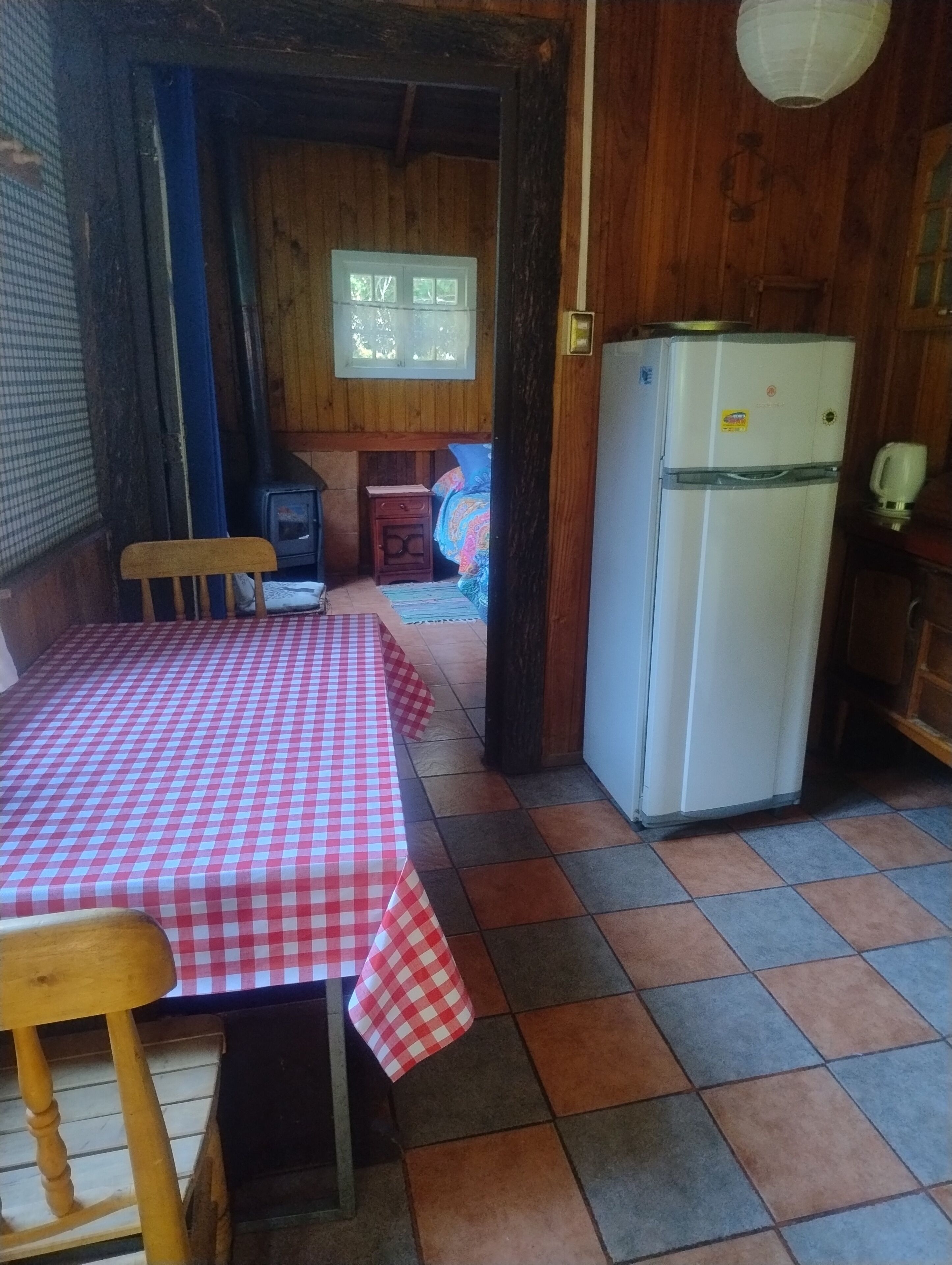 A room with a checkered table, a refrigerator, a window, and a wooden wall.