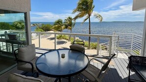 A balcony with a glass table and chairs, overlooking a beach with palm trees and the ocean. - Amazing Ocean Front Views 3 bedroom / bath Villa. Wake up to a Sunrise (Key Largo)