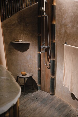 A bathroom with a wooden floor, a bamboo shower, a small stool with a bowl, and a towel hanging on the wall. - The Kul Kul Farm (Abiansemal)