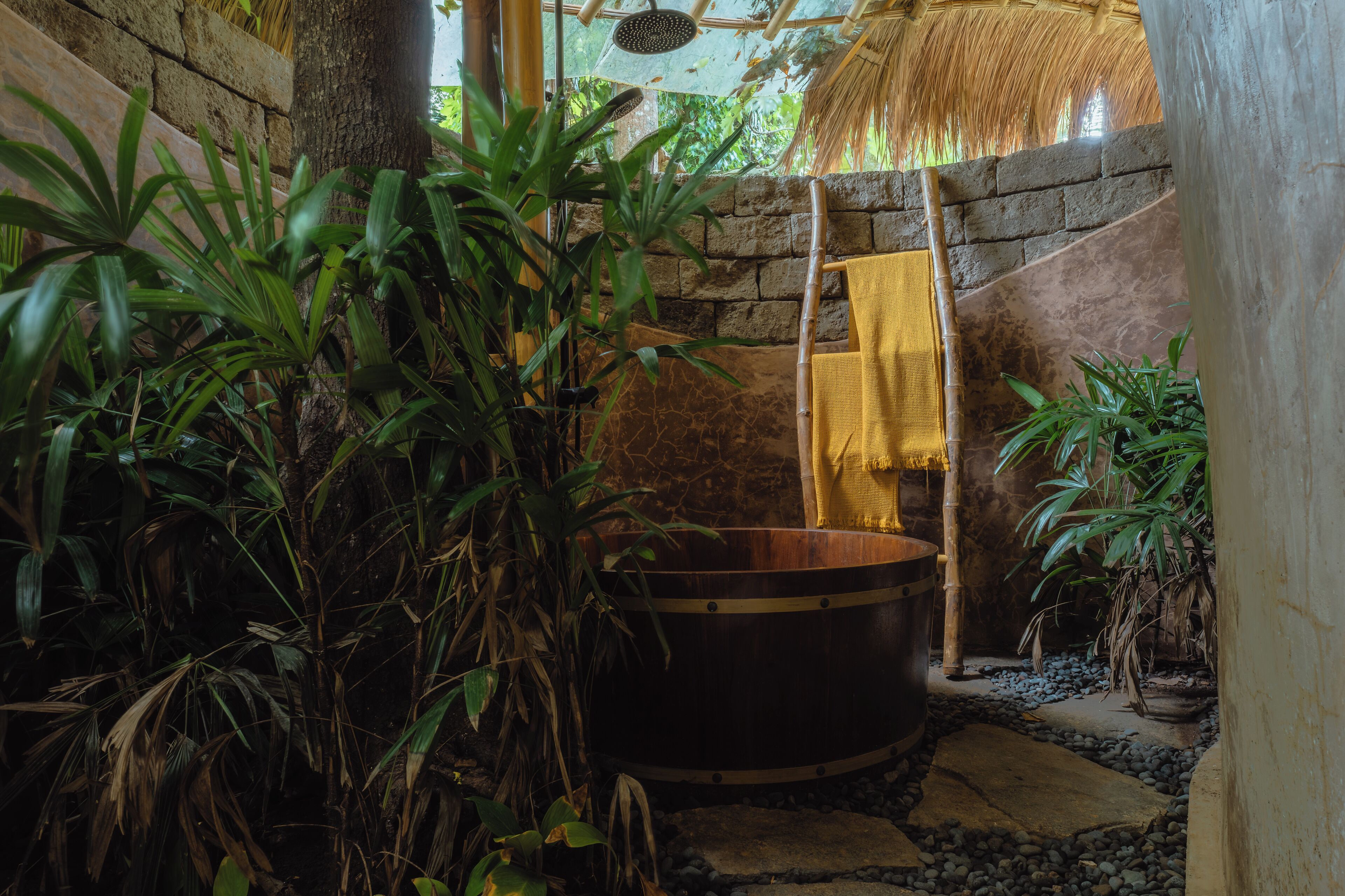 A traditional wooden bathtub in a natural setting with stone walls and lush greenery.
