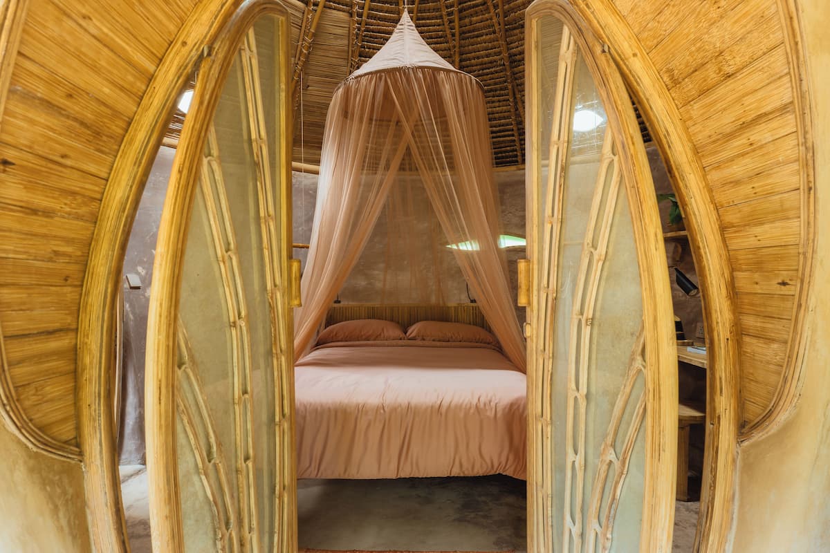 A room with a bed under a canopy, wooden walls, and a ceiling with a woven design.