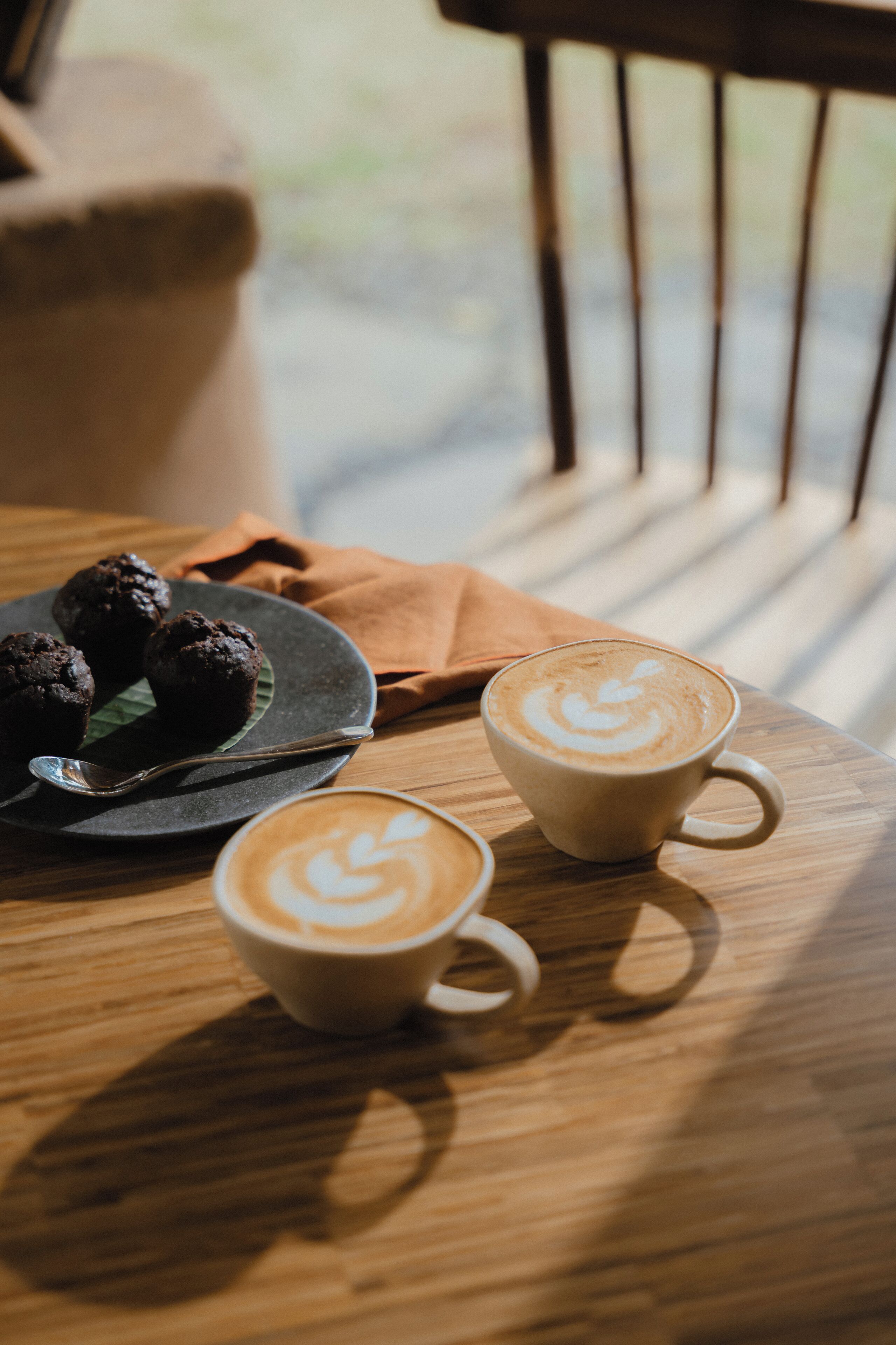 Ein Holztisch mit zwei Kaffeetassen und einem Teller mit Muffins.