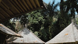 A traditional wooden structure with a circular window and a thatched roof, surrounded by lush greenery. - The Kul Kul Farm (Abiansemal)