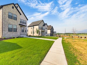 A row of modern two-story houses with stone facades, a well-maintained lawn, and a clear sky.