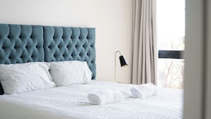 A neatly made bed with white bedding and a blue tufted headboard.