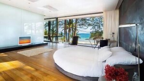 Un dormitorio moderno con una cama curvada, ventanas amplias y vista a la playa.