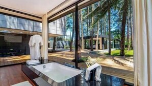Un baño moderno con una bañera grande, una ducha con cerramiento de vidrio y vistas a una zona boscosa.