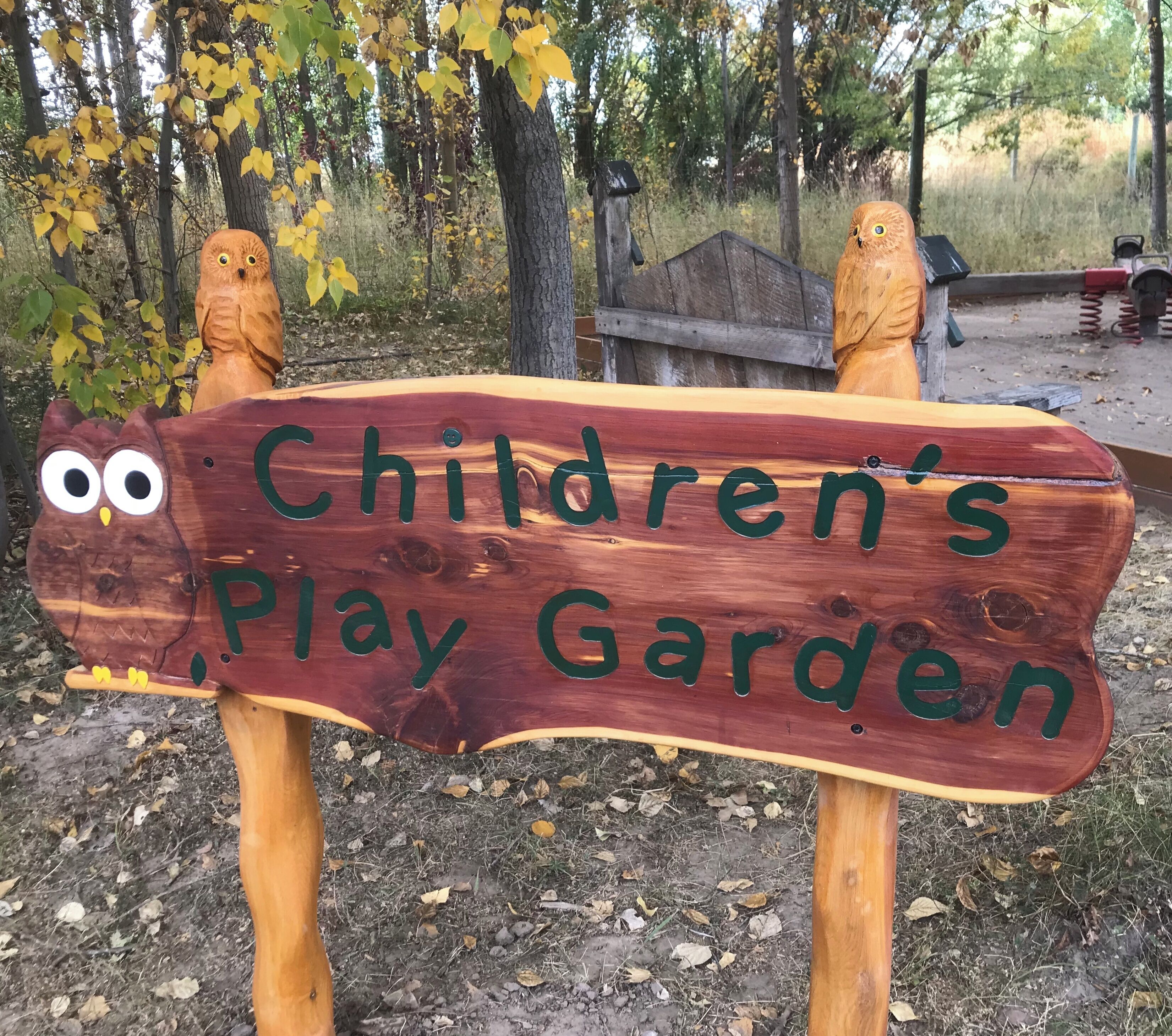 Un cartello di legno con intagli di gufi e la scritta 'Children's Play Garden'.