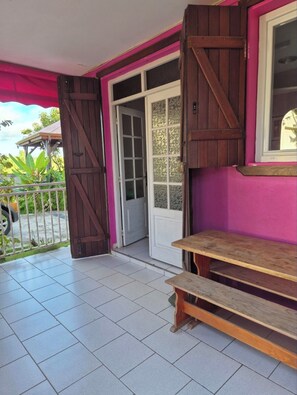 A covered outdoor area with a wooden bench, a door with glass panels, and a pink wall.
