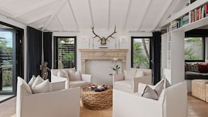 Un salon spacieux avec une cheminée, des canapés blancs et une grande fenêtre donnant sur un jardin.