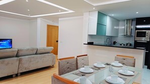 Een moderne woonkamer met een bank, een televisie en een eetgedeelte met een tafel voor vier personen.