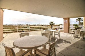 Un patio al aire libre con mesas y sillas redondas, una cerca blanca y un letrero de 'No Fumar'.