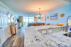 A kitchen with a large island, a dining area with chairs, a ceiling fan, and a view of the outdoors.
