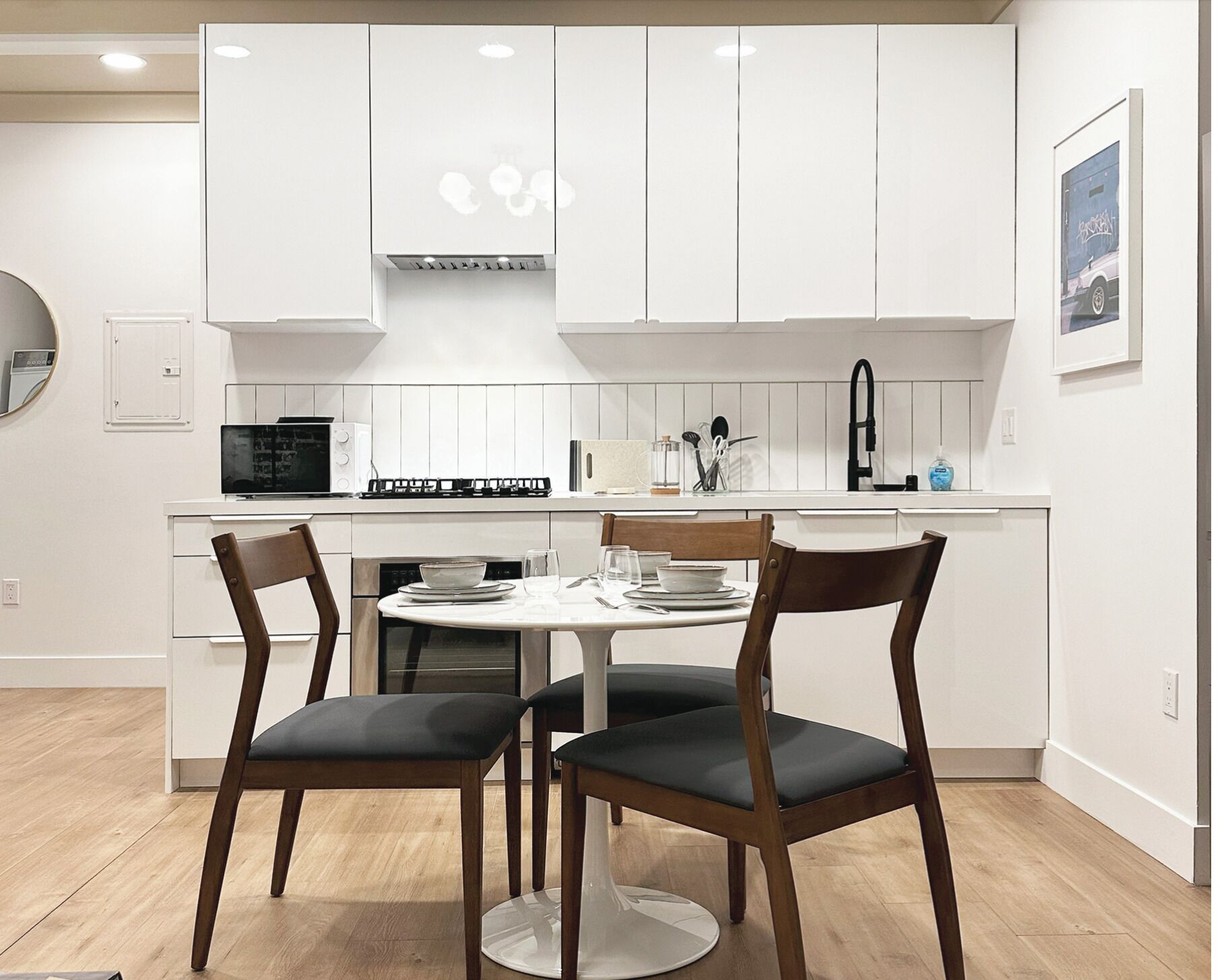 A modern kitchen with white cabinets, a round dining table, and two chairs.