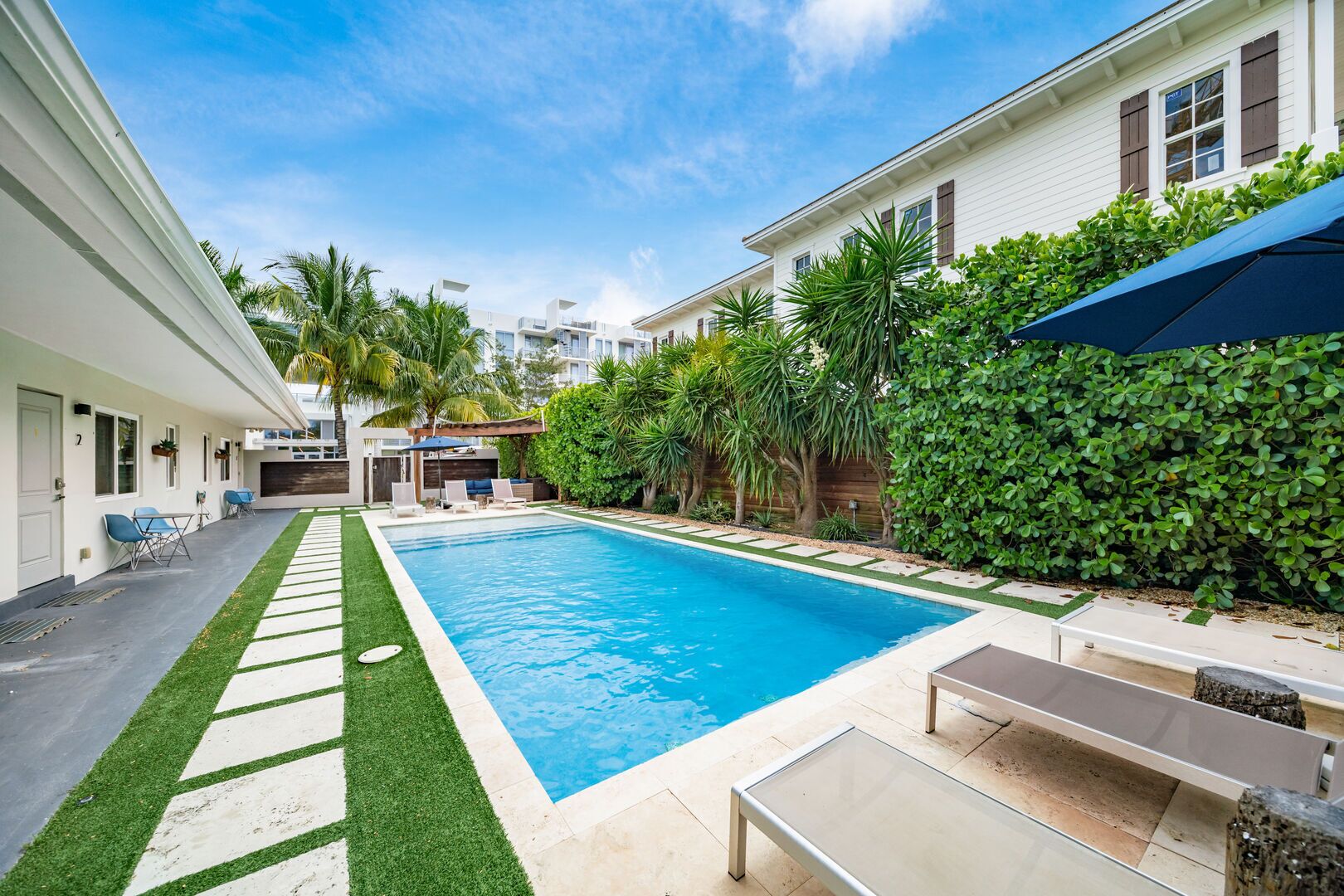 A swimming pool with a surrounding deck, a covered seating area, and a view of adjacent buildings.