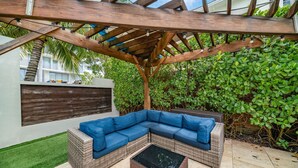 An outdoor seating area with a blue sectional sofa and a small table, under a wooden pergola.
