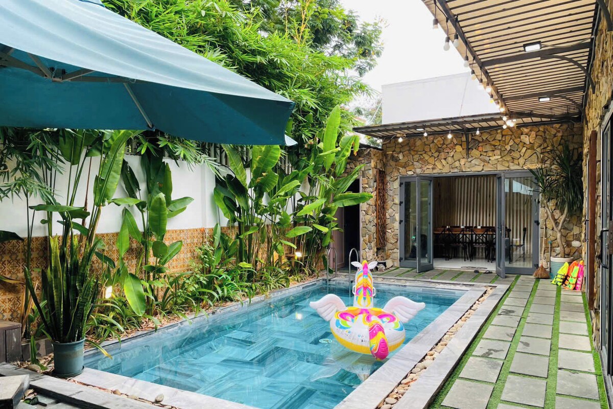 A swimming pool with two inflatable toys, surrounded by lush greenery and a stone wall.