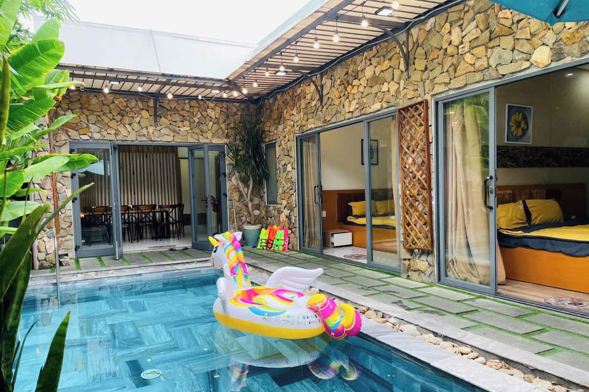 A swimming pool with inflatable toys, a stone wall, and a glass door leading to a bedroom.