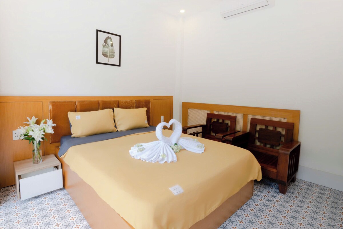 A hotel room with a bed, a nightstand, a chair, and a wall-mounted air conditioner.