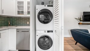 A compact kitchen with white cabinets, a green tiled backsplash, and a Samsung washing machine.