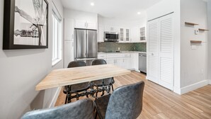 A modern kitchen with white cabinets, a stainless steel refrigerator, a microwave, and a dining area with a wooden table and chairs.