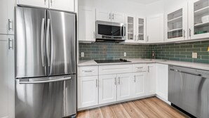 A modern kitchen with stainless steel appliances, white cabinetry, a green tiled backsplash, and a wooden floor.