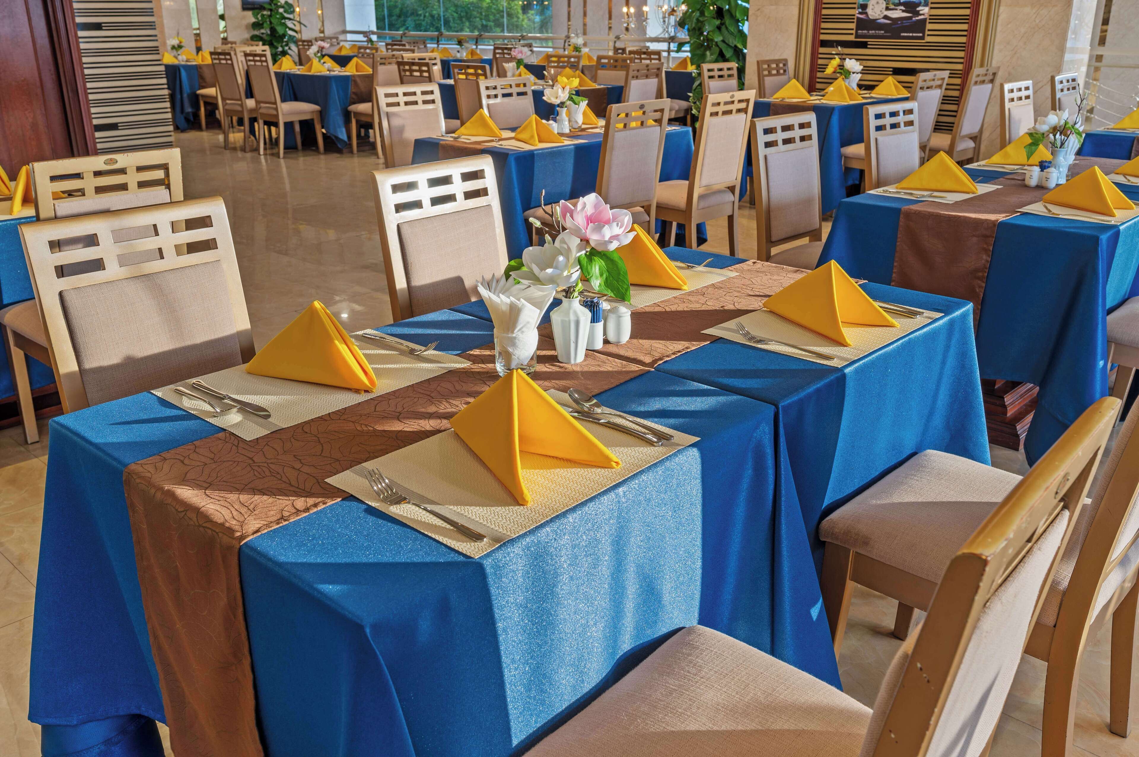 Un espace repas avec des tables dressées pour accueillir plusieurs convives, agrémenté de nappes bleues et de serviettes jaunes.