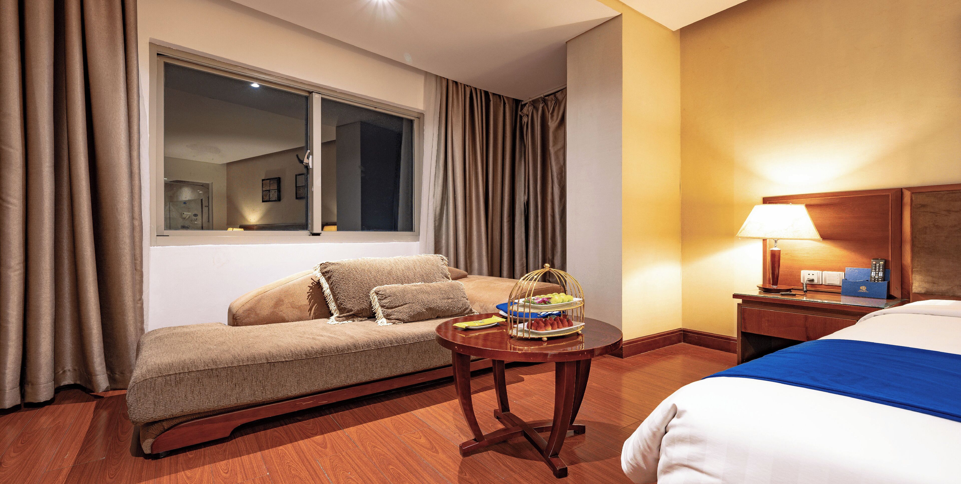 Una habitación de hotel con un sofá, una mesita con una cesta de fruta, una lámpara y una cama.