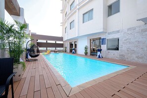 A swimming pool with a wooden deck, surrounded by potted plants and a hanging chair. - Sandals Stay Hotel (Hai Chau)