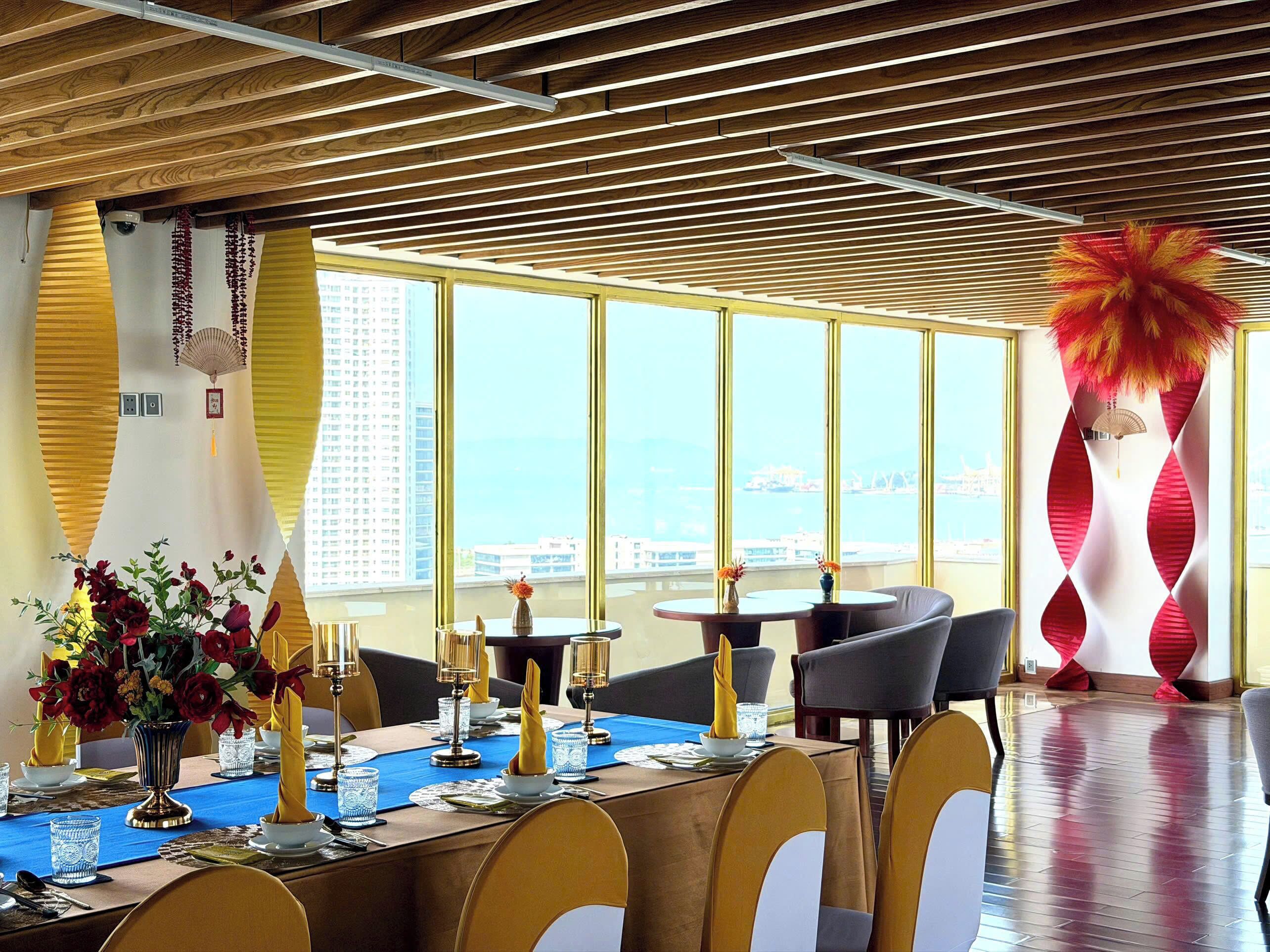 A dining area with a long table set for a meal, large windows with a view of the city, and a decorative red feather sculpture.