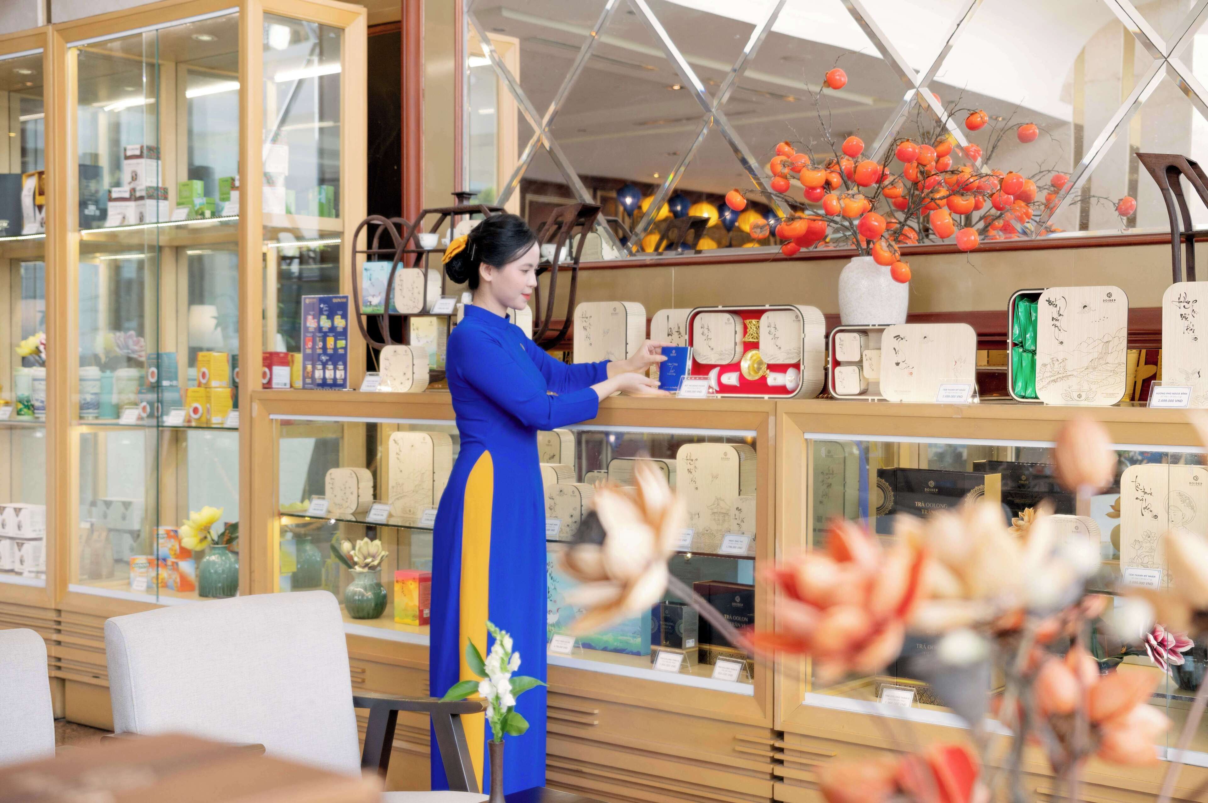 A woman in a blue dress arranging items on a counter in a shop with glass display cases.