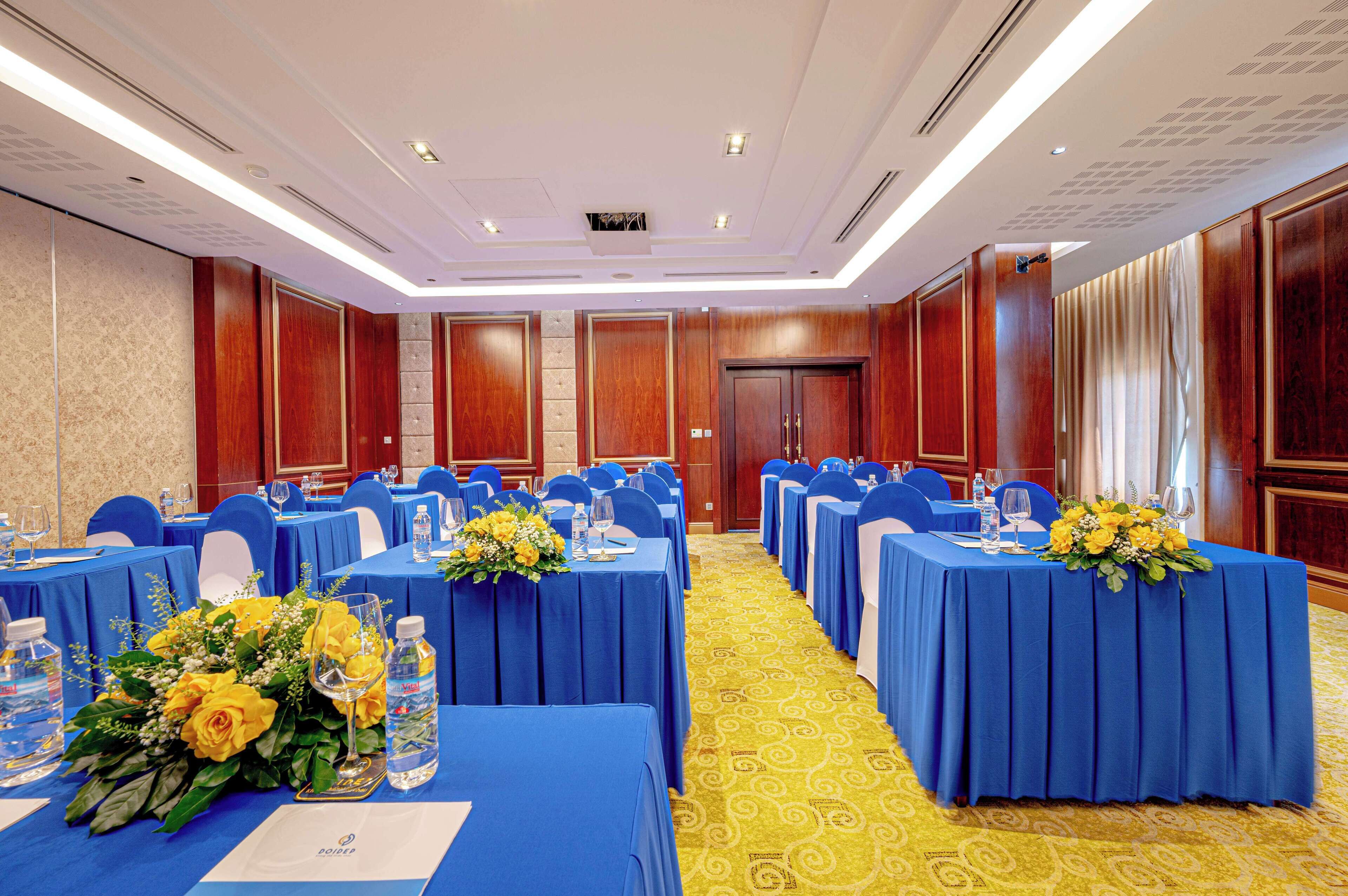 A conference room with rows of tables, blue tablecloths, and yellow carpeting.