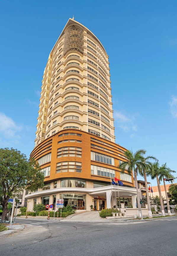 A tall, curved hotel with multiple floors, a prominent entrance, and palm trees in the foreground. - Sandals Stay Hotel (Hai Chau)