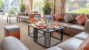 A well-lit, elegantly furnished lounge area with a sofa set, a coffee table with decorative items, and a view of the cityscape through large windows. - Sandals Stay Hotel (Da Nang)
