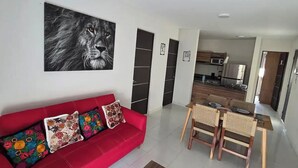 En stue med en rød sofa, et spisebord med stole, et køkken i baggrunden og en loftventilator.