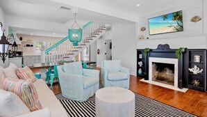 Un salon spacieux avec un escalier, des fauteuils bleu clair, un canapé blanc et une cheminée.