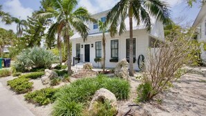 Une maison à deux étages, à l’extérieur blanc, entourée d’un jardin tropical comprenant des palmiers et divers arbustes.