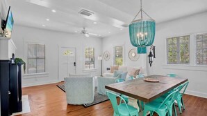 Une pièce spacieuse avec une table à manger en bois, des chaises de couleur turquoise, un lustre turquoise suspendu et un ventilateur de plafond.