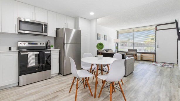 A modern kitchen with white cabinets, stainless steel appliances, and a dining area with white chairs and a round table.